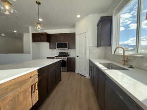 Kitchen with backsplash, sink, decorative light fixtures, light hardwood / wood-style floors, and stainless steel appliances