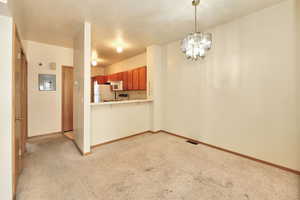 Kitchen with kitchen peninsula, white appliances, light colored carpet, and a notable chandelier