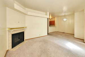 Unfurnished living room featuring a tile fireplace, a chandelier, and light colored carpet