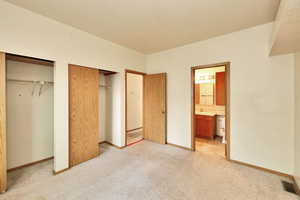 Unfurnished bedroom with ensuite bathroom and light carpet