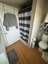 Bathroom featuring wood-type flooring, a textured ceiling, toilet, and walk in shower