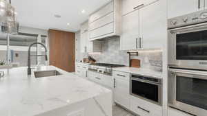 Kitchen with appliances with stainless steel finishes, light stone counters, custom exhaust hood, sink, and pendant lighting