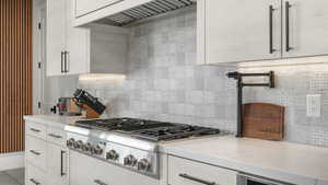 Kitchen featuring white cabinetry, light stone countertops, premium range hood, and stainless steel gas cooktop