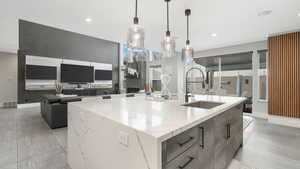 Kitchen featuring hanging light fixtures, a large island, sink, and light stone counters