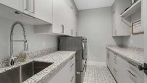 Clothes washing area featuring sink, light tile patterned floors, cabinets, and independent washer and dryer