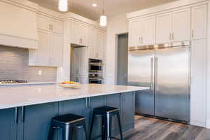 Kitchen with decorative backsplash, premium range hood, stainless steel appliances, dark wood-type flooring, and hanging light fixtures