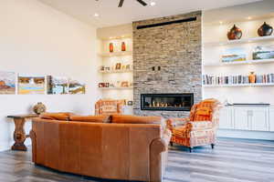 Living room with built in shelves, hardwood / wood-style flooring, a stone fireplace, and ceiling fan