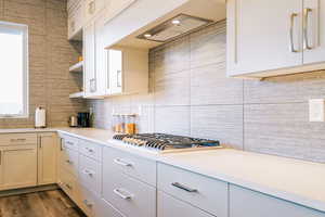 Kitchen with ventilation hood, dark hardwood / wood-style floors, decorative backsplash, and stainless steel gas cooktop