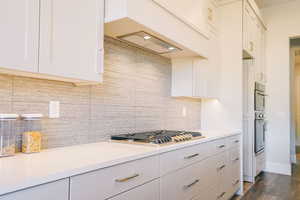 Kitchen featuring dark hardwood / wood-style flooring, white cabinetry, stainless steel gas stovetop, and backsplash