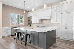 Kitchen with decorative light fixtures, premium range hood, white cabinetry, a kitchen island, and stainless steel appliances