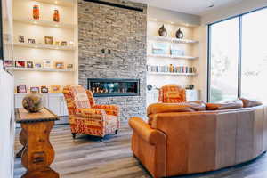 Living room with built in features, a stone fireplace, and light wood-type flooring