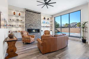 Living room featuring wood-type flooring, built in features, ceiling fan, and a stone fireplace