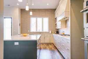 Kitchen with stainless steel gas stovetop, custom range hood, dark wood-type flooring, white cabinets, and hanging light fixtures