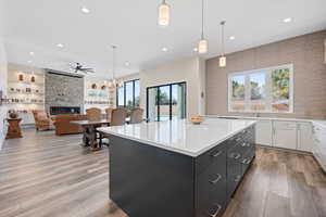 Kitchen featuring a kitchen island, white cabinetry, a stone fireplace, light hardwood / wood-style floors, and hanging light fixtures