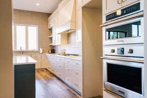 Kitchen featuring custom exhaust hood, sink, light hardwood / wood-style floors, white cabinetry, and stainless steel appliances