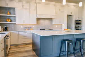 Kitchen with custom exhaust hood, decorative backsplash, appliances with stainless steel finishes, decorative light fixtures, and a breakfast bar area