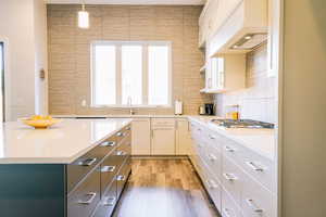 Kitchen with white cabinets, pendant lighting, hardwood / wood-style floors, and custom exhaust hood