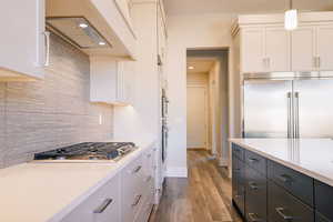 Kitchen with backsplash, white cabinets, hanging light fixtures, appliances with stainless steel finishes, and wood-type flooring