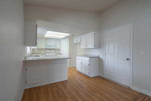 Kitchen with white appliances, sink, kitchen peninsula, light wood-type flooring, and white cabinetry