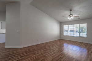 Unfurnished room featuring a textured ceiling, ceiling fan, lofted ceiling, and dark wood-type flooring