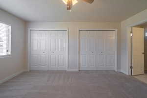 Unfurnished bedroom featuring a textured ceiling, ceiling fan, light carpet, and two closets