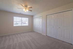 Unfurnished bedroom with ceiling fan, light colored carpet, a textured ceiling, and two closets