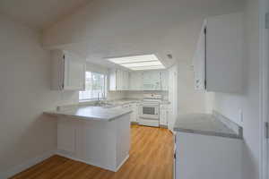 Kitchen with white appliances, white cabinets, sink, light hardwood / wood-style flooring, and kitchen peninsula