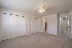 Unfurnished bedroom featuring multiple closets, ceiling fan, ensuite bathroom, light colored carpet, and a textured ceiling