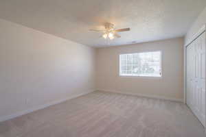 Unfurnished bedroom with a textured ceiling, ceiling fan, light carpet, and a closet