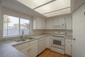 Kitchen with white appliances, light hardwood / wood-style flooring, white cabinetry, and sink