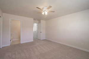 Unfurnished bedroom with a textured ceiling, light colored carpet, ensuite bath, and ceiling fan