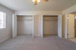 Unfurnished bedroom with light carpet, a textured ceiling, two closets, and ceiling fan