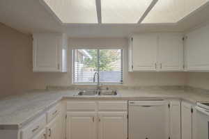 Kitchen featuring white dishwasher, white cabinets, and sink