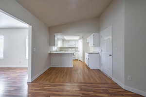 Kitchen featuring hardwood / wood-style floors, lofted ceiling, white appliances, kitchen peninsula, and white cabinetry