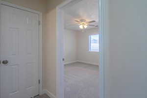 Hallway with a textured ceiling and light colored carpet