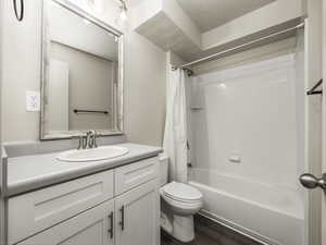 Full bathroom featuring hardwood / wood-style floors, vanity, shower / bath combination with curtain, toilet, and a textured ceiling