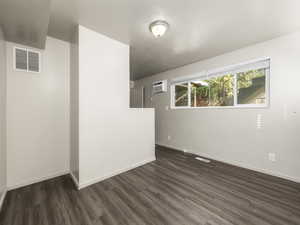 Empty room featuring dark hardwood / wood-style flooring, a textured ceiling, and a wall mounted AC