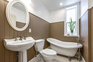 Bathroom featuring tile patterned flooring, toilet, a tub, and wood walls