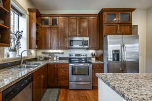 Kitchen featuring hardwood / wood-style floors, light stone counters, sink, and appliances with stainless steel finishes