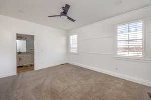 Unfurnished bedroom featuring ensuite bath, ceiling fan, and medium colored carpet