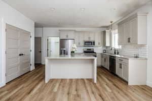 Kitchen with appliances with stainless steel finishes, light stone counters, pendant lighting, light hardwood / wood-style floors, and a kitchen island