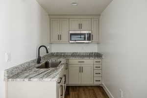 Kitchen featuring light stone counters, sink, dark wood-type flooring, and a textured ceiling