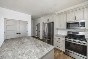 Kitchen with a center island, backsplash, appliances with stainless steel finishes, light hardwood / wood-style floors, and light stone counters