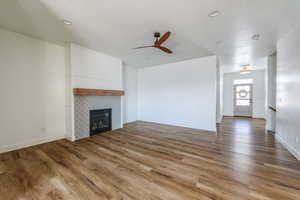 Unfurnished living room with a tiled fireplace, ceiling fan, and wood-type flooring