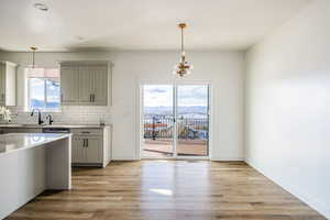 Kitchen featuring gray cabinetry, hanging light fixtures, light wood-type flooring, tasteful backsplash, and a chandelier