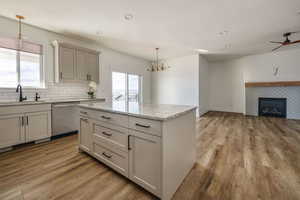 Kitchen with dishwasher, sink, hanging light fixtures, light hardwood / wood-style floors, and a tiled fireplace