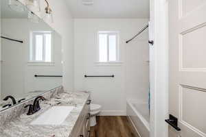 Full bathroom with toilet, vanity, a healthy amount of sunlight, and hardwood / wood-style flooring