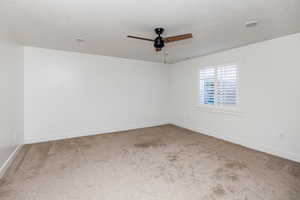 Empty room with ceiling fan, carpet, and a textured ceiling