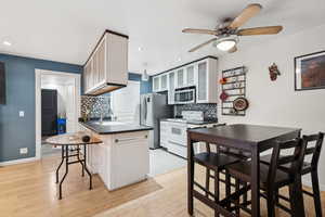 Kitchen featuring a kitchen breakfast bar, white cabinetry, light hardwood / wood-style flooring, and stainless steel appliances