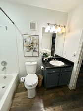 Full bathroom with washtub / shower combination, toilet, vanity, and wood-type flooring